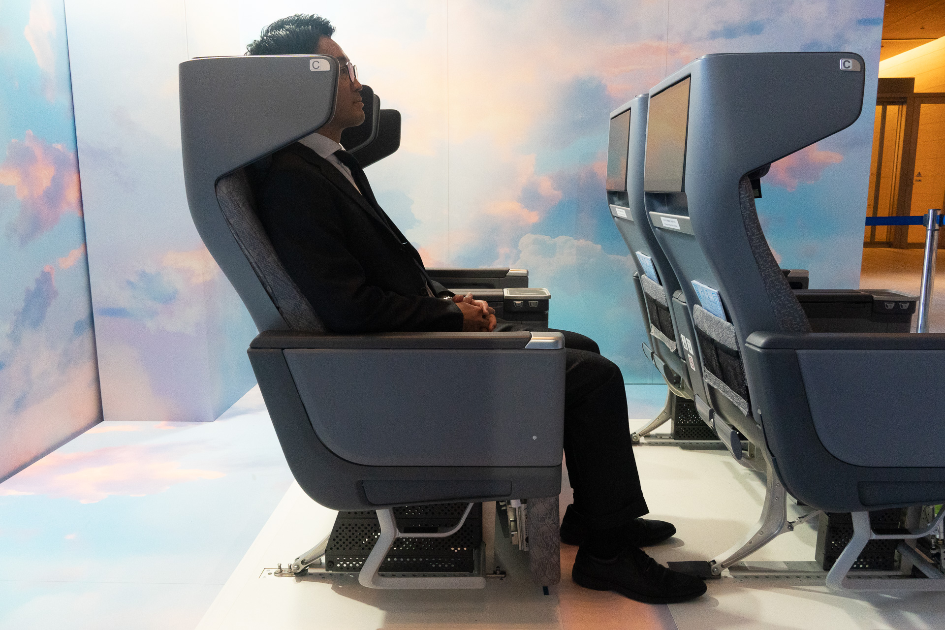 An adult male seated, demonstrating the generous space between his seat and the one in front.