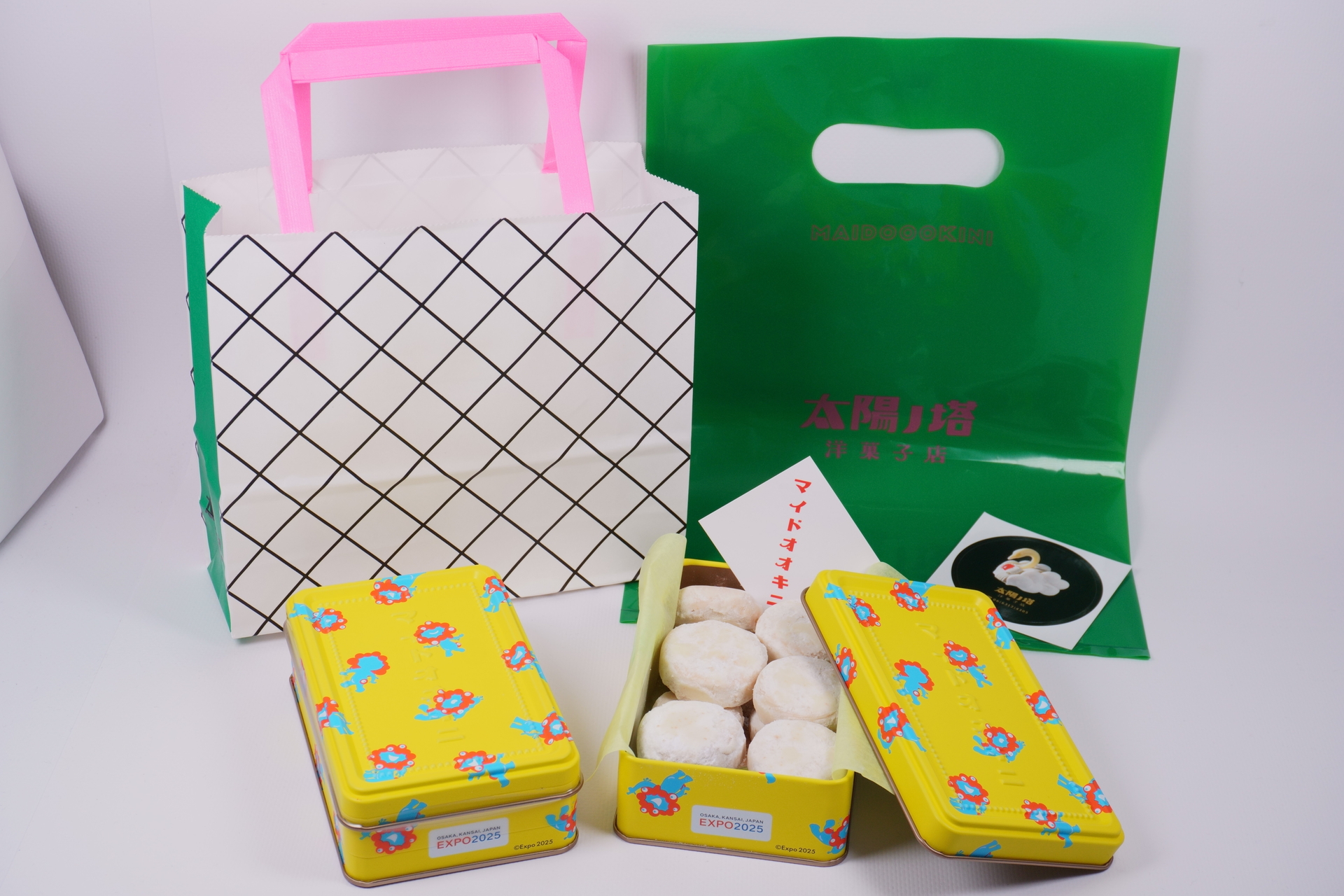購入したマイドオオキニ缶（イエロー）。後ろに並んでいるのが、紙袋とビニール袋
