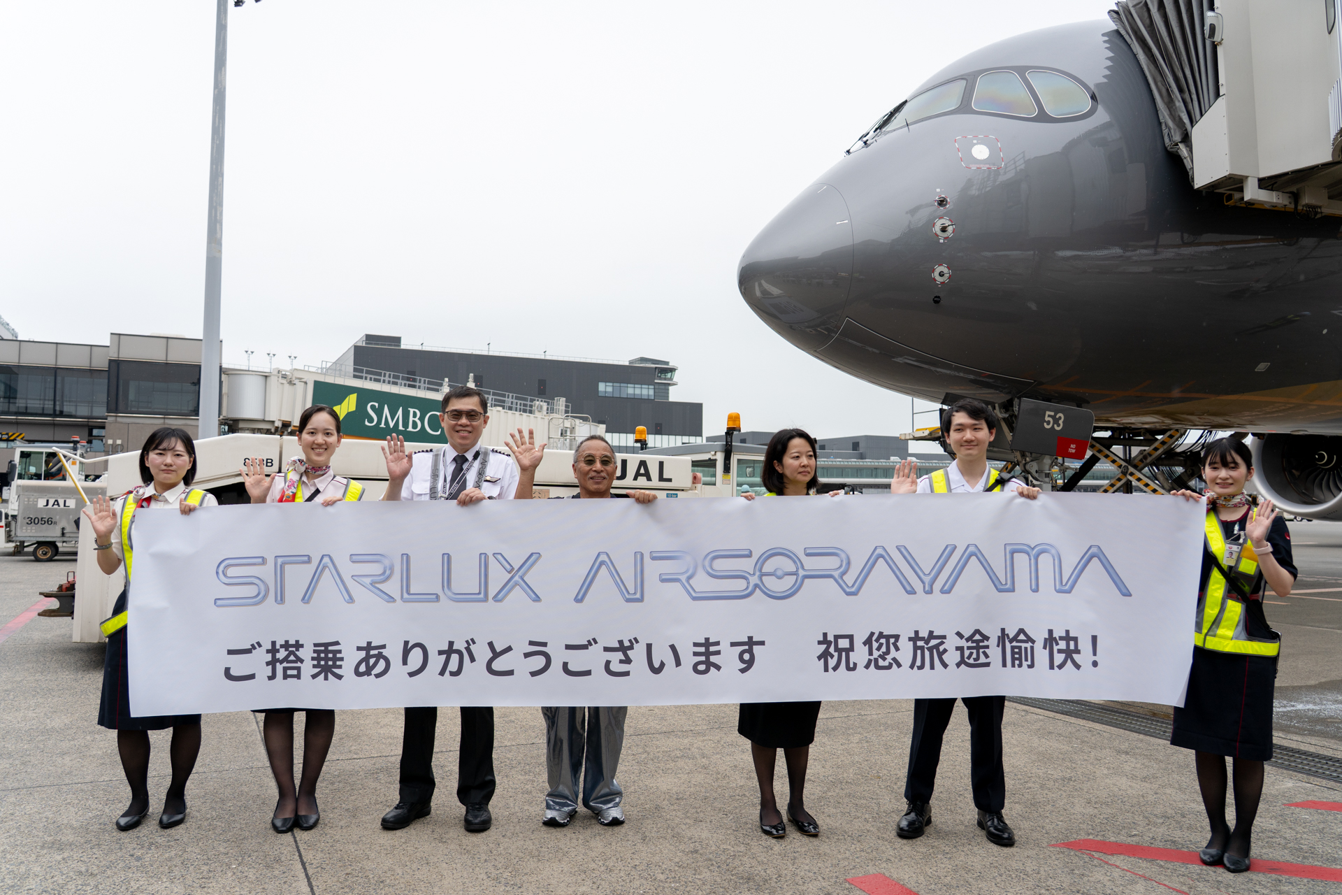 折り返し便の出発を前に、駐機場で特別横断幕を掲げるスタッフの輪に加わるスターラックス航空の張会長（左から3人目）と空山基氏（中央）