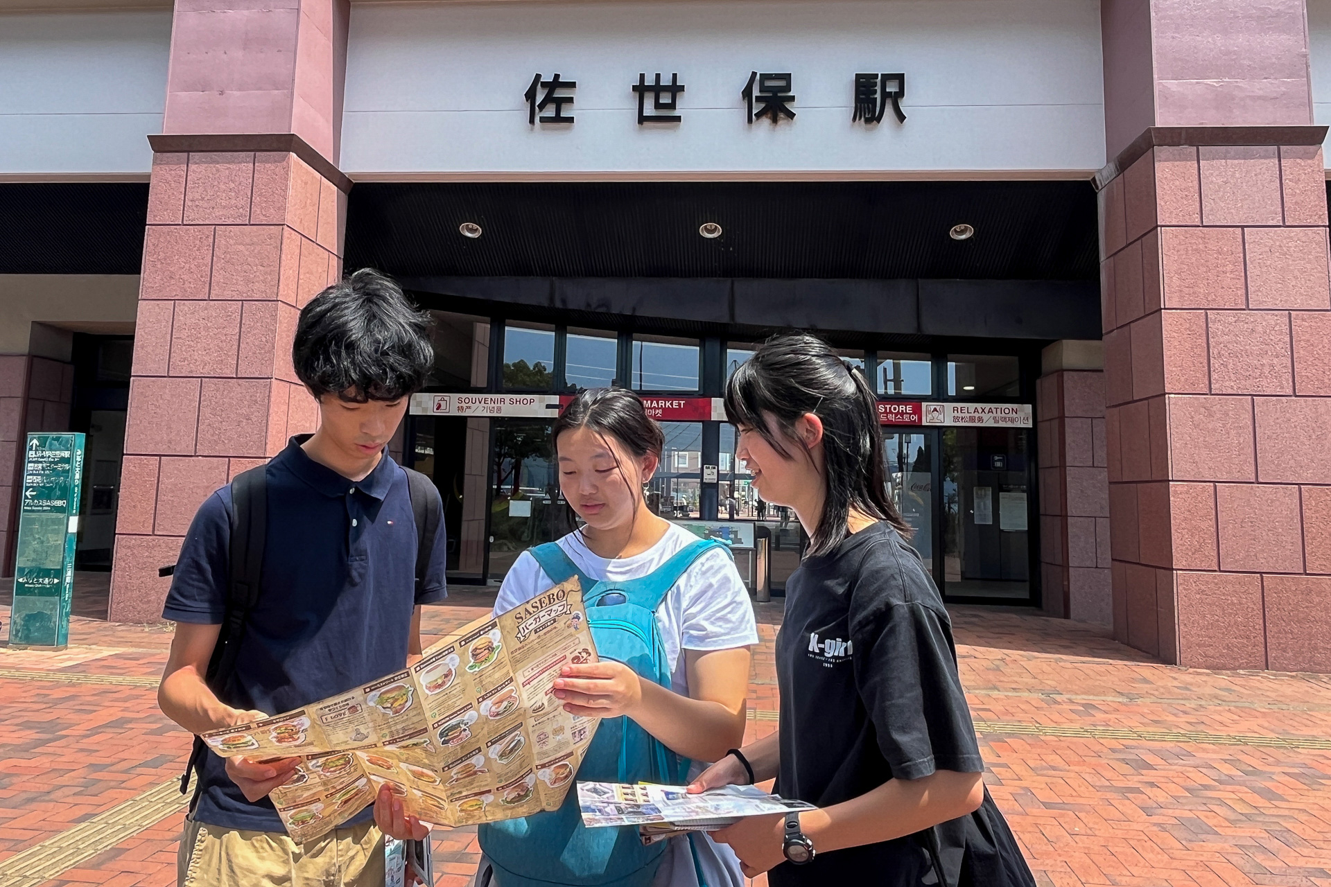 佐世保駅前で地図を広げる公共交通機関チーム。佐世保バーガーや鯨肉を食べたり、松浦鉄道に乗車しながら少し遅れて的山大島入り