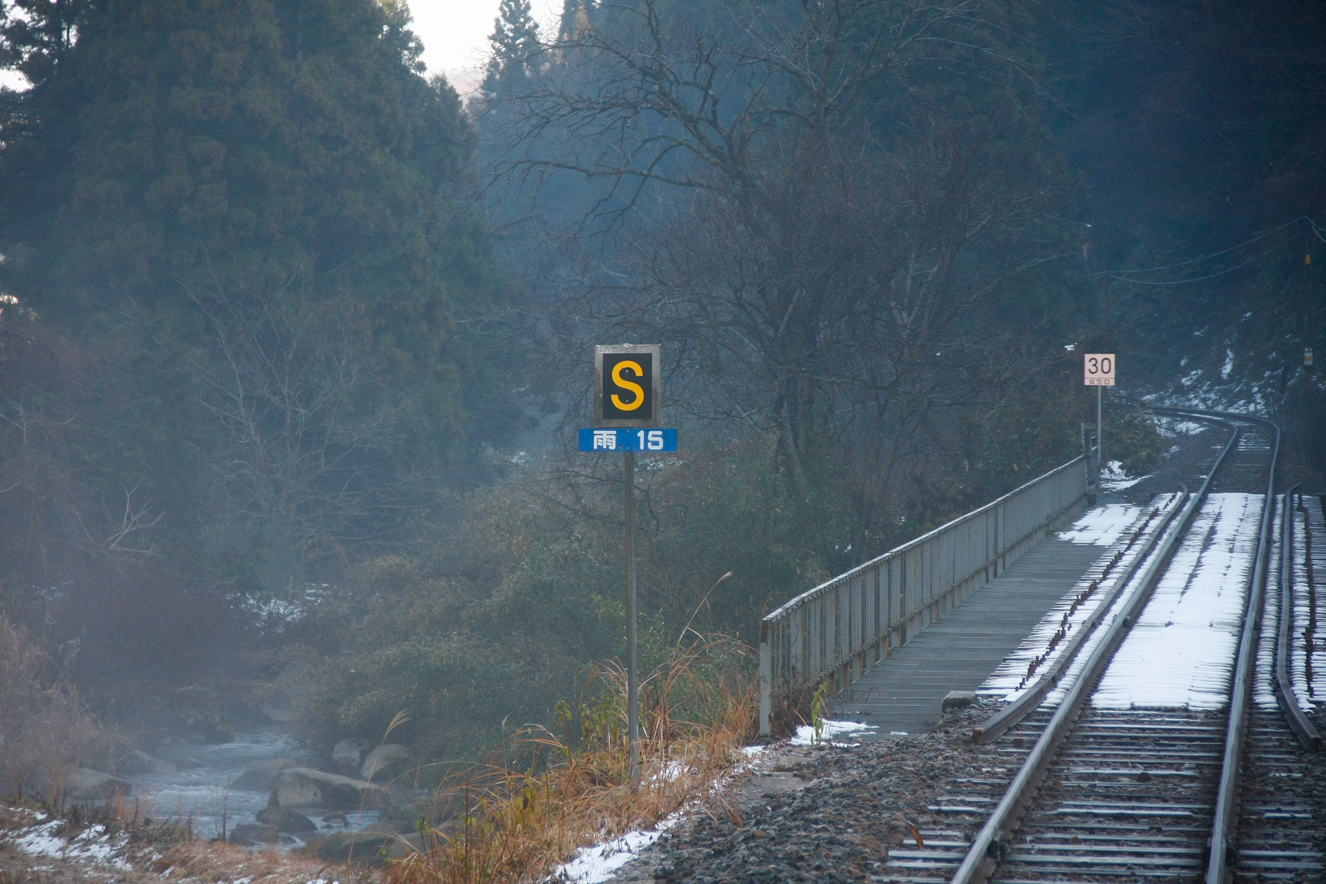 木次線で。奥の方に「ここから650mの間は30km/h制限」との標識が建っているが、その手前の橋梁でも、雨が降ったら15km/hに規制している