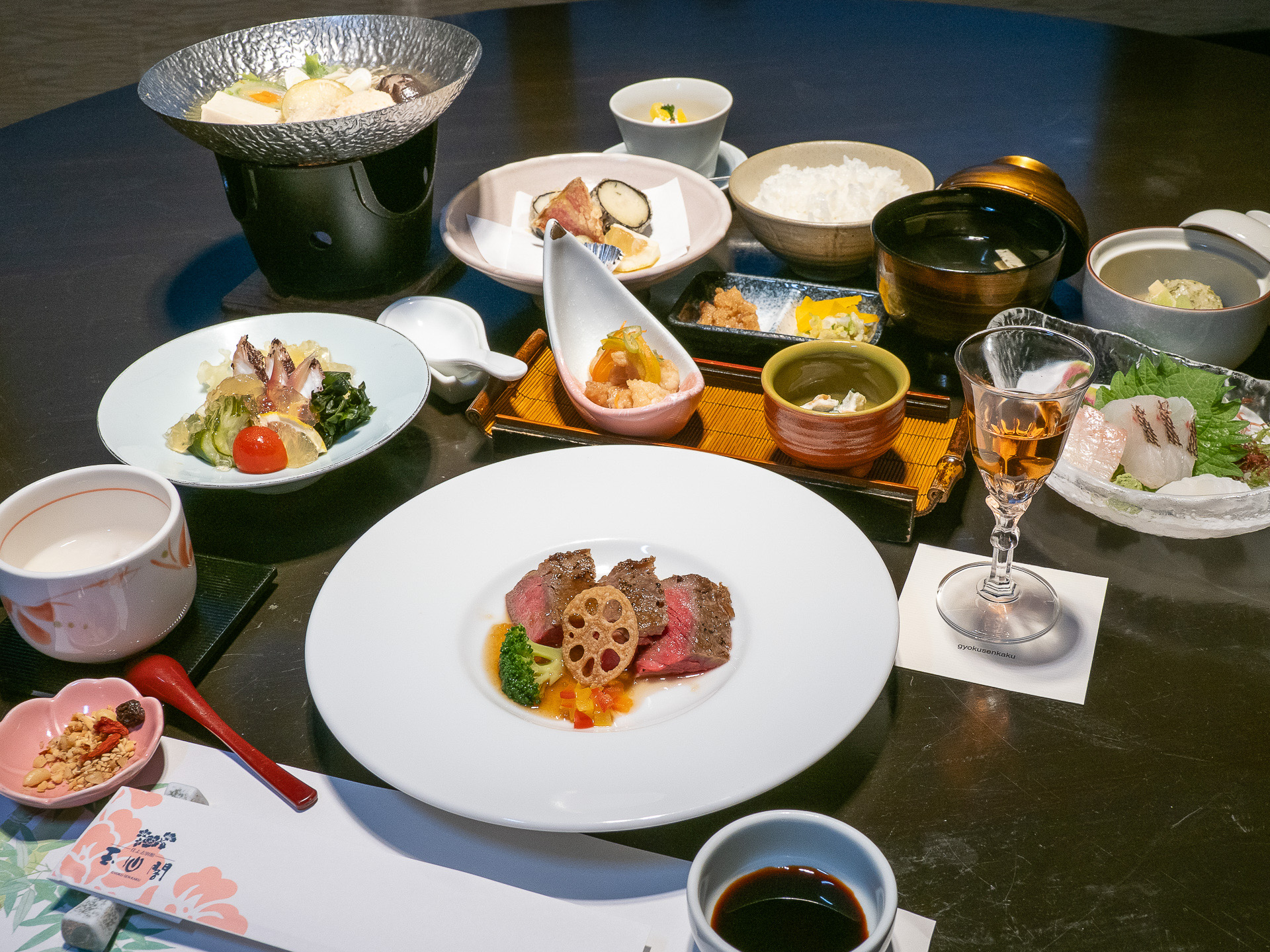 夕食のおしながきは、食前酒 楊貴妃ワイン、先付 季節の前菜二種、造里 本日のお勧め三種盛合わせ あしらい一式、鍋物 長州鶏のつみれと季節野菜のゆずきち薫る出汁鍋、酢の物 蛸と胡瓜のマリネ土佐酢ジュレ掛け、薬膳粥 ラバジュー、洋皿 厳選国産牛ロースステーキ彩り野菜添え、替鉢 あおさ道明寺、季節野菜の銀餡かけ、油物 帆立貝柱と紫蘇の磯辺揚げ季節の野菜添え、御飯 山口県産きぬむすめ じゃこ味噌 漬物、止椀 旬のつみれ 青味ほか、デザート ゆずきちゼリー