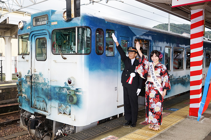 城崎温泉駅にて「天空の城 竹田城跡号」の出発合図をする西日本旅客鉄道株式会社 城崎温泉駅長 岩本昭信氏と城崎温泉観光大使 月島ほたるさん
