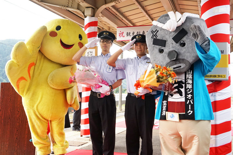 花束贈呈式の兵庫県マスコットキャラクター「はばたん」、福知山車掌区所属 尾崎貴紀車掌、豊岡車掌区所属 椿野絋平運転士、豊岡市マスコットキャラクター「玄武岩の玄さん」