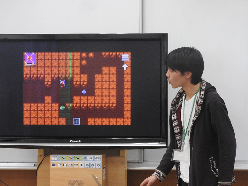 「HackforPlay」の解説を行っている寺本氏。画面はオーソドックスなRPGのようだが、ダンジョンの中に落ちている魔道書を拾うことで、ゲームのプログラムをハックできる