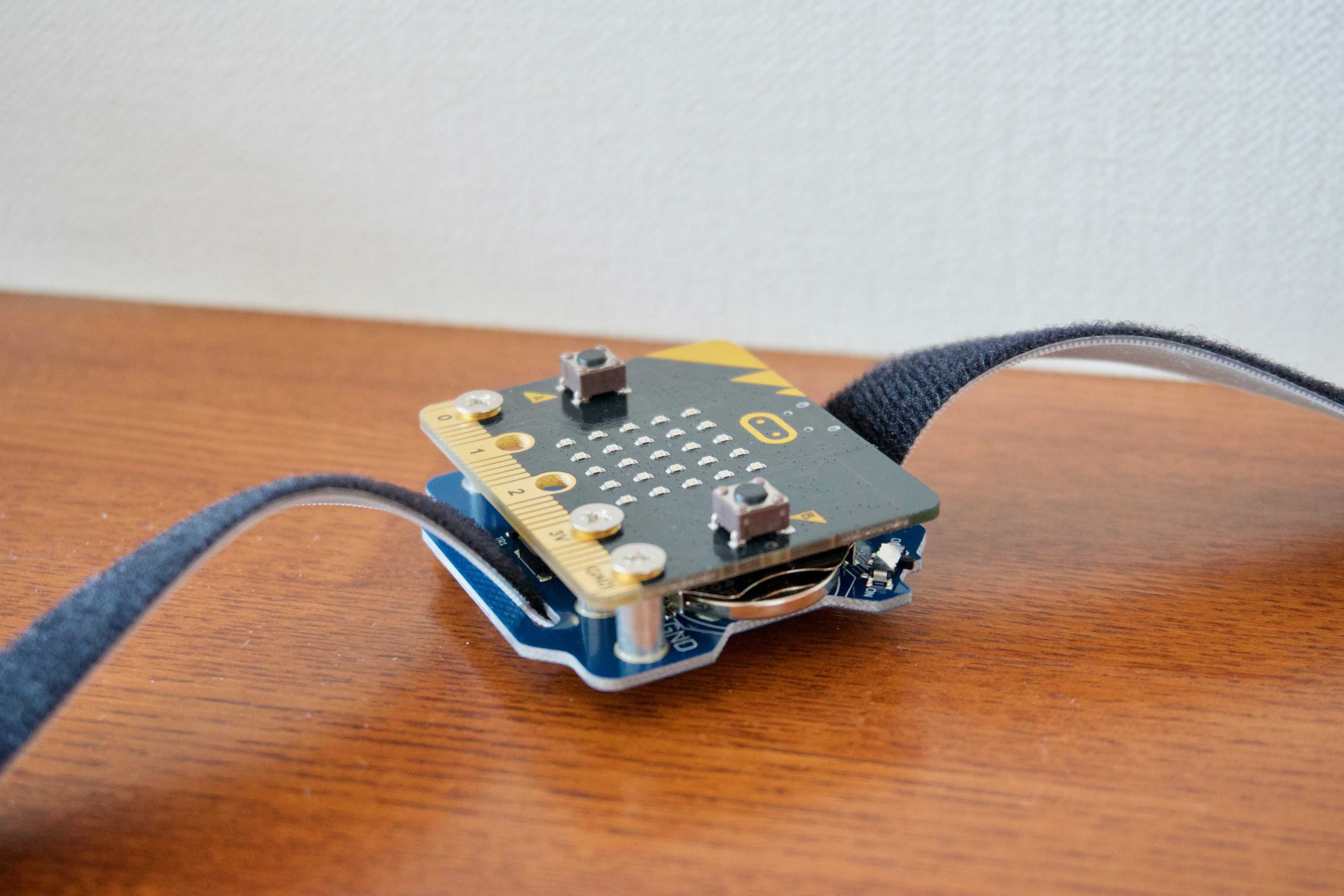 身に着けるには、ボタン電池を使えるバングルモジュールが便利。micro:bitと重ねてねじ止めし、マジックテーブが通せる。腕時計のように手に巻きつけられる