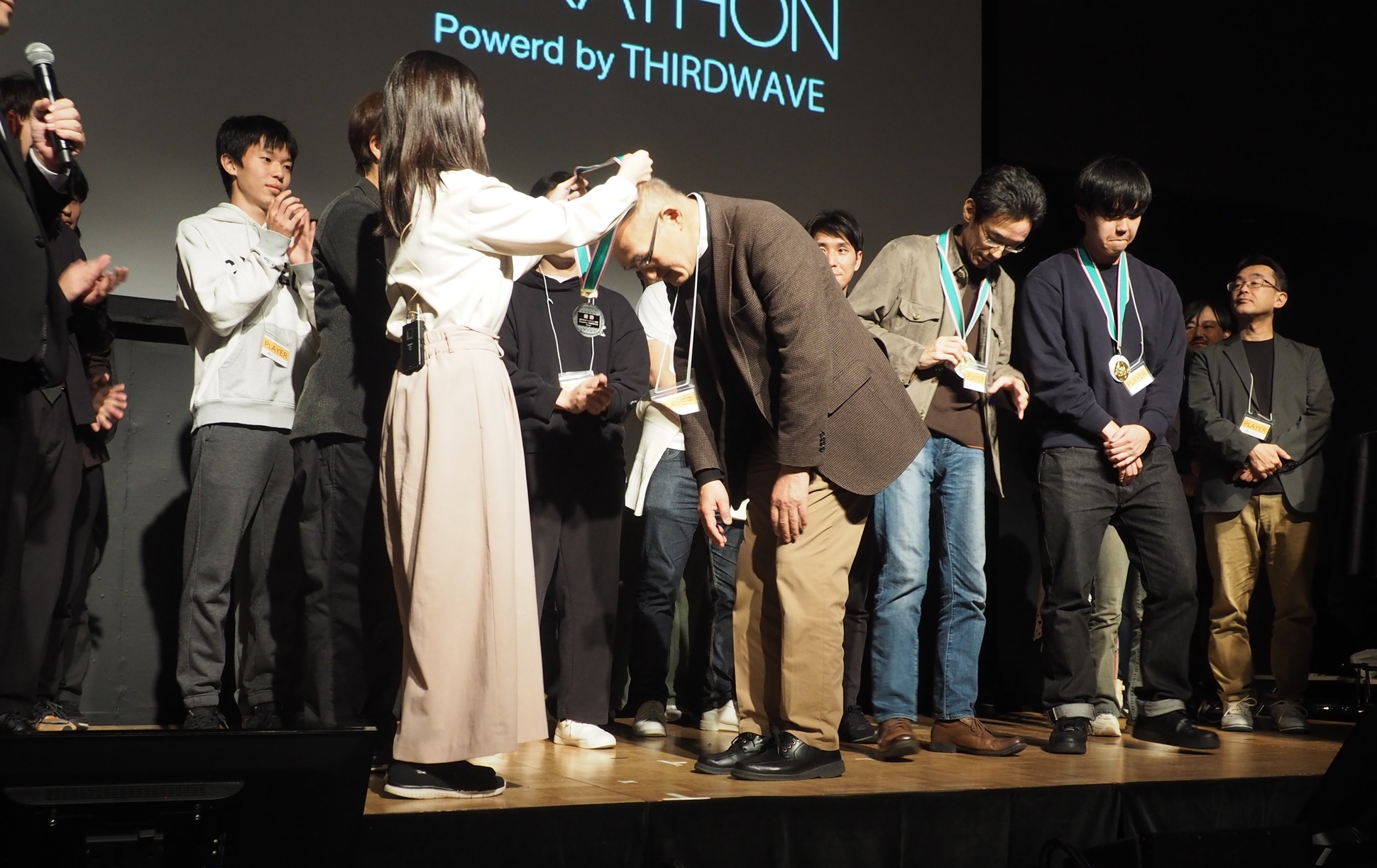 「たい焼きテクノロジーズ」の3人目のメンバーの首にメダルをかけた